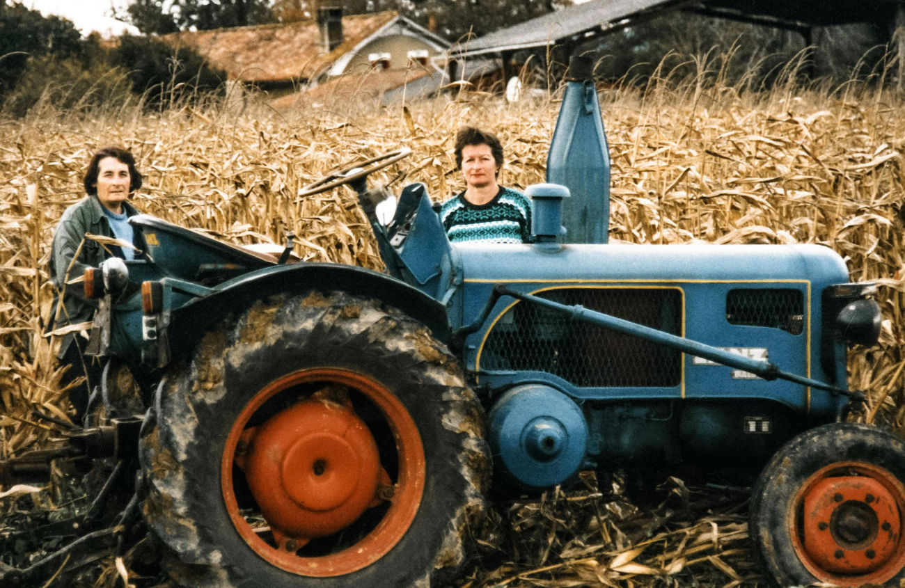 Two ladies in the fields, in the process of cultivation and gathering, next to a tractor. An image representing the work from sowing to harvest.