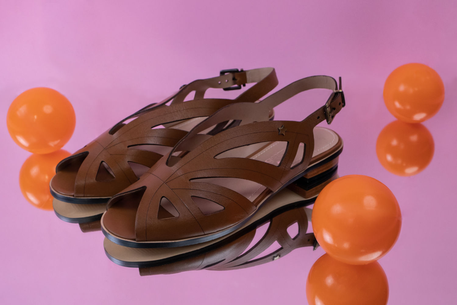 Fotografia de estúdio: calçado sobre superfície rosa com esferas cor de laranja.